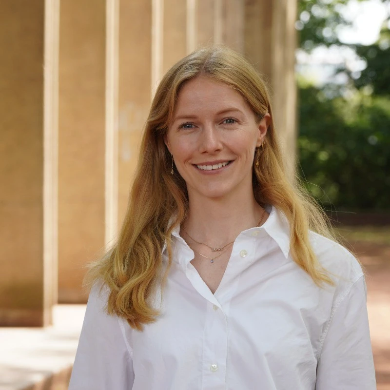 Portrait of Catharina Michels, smiling in a white shirt in front of sandstone columns